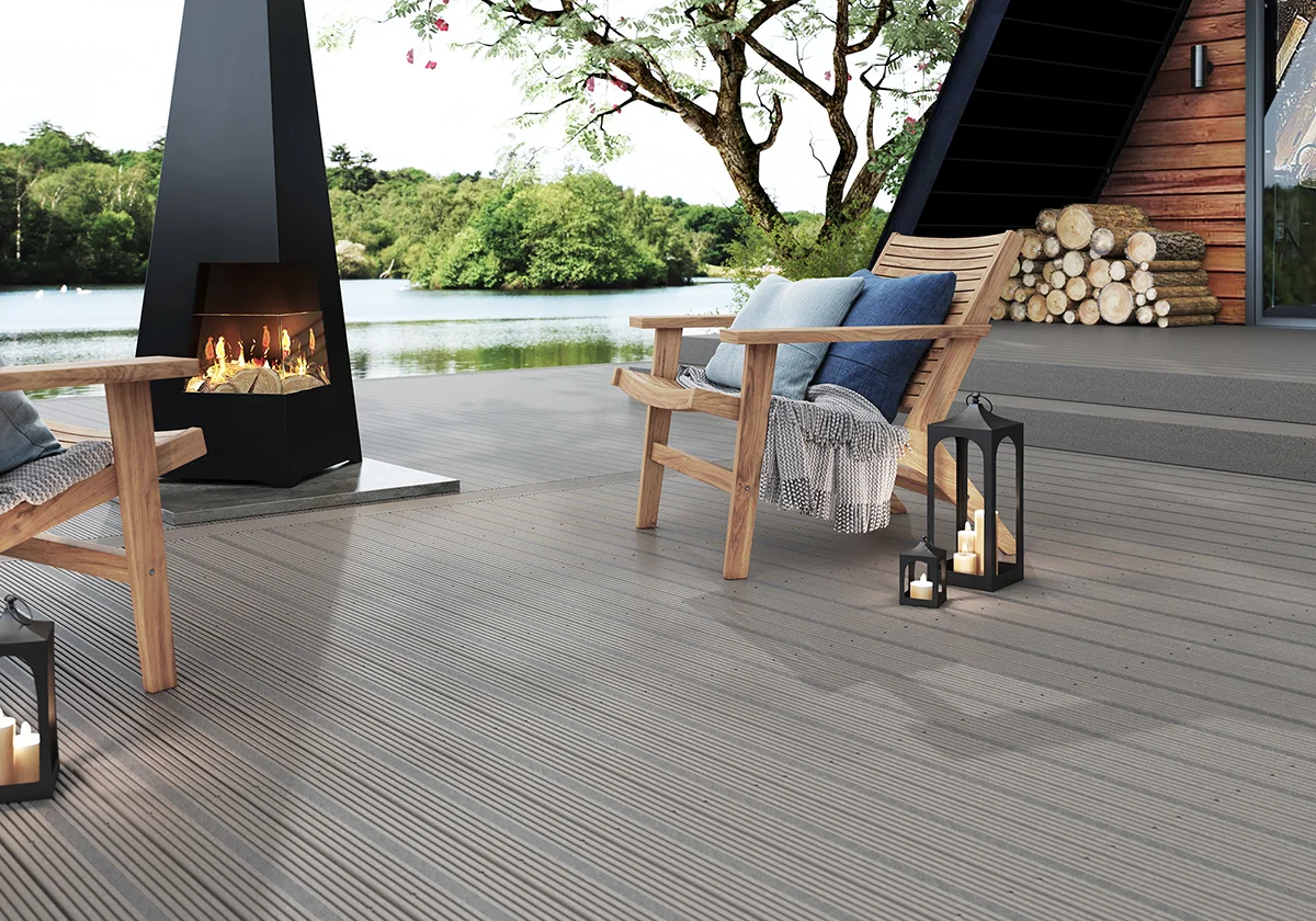 Two wooden chairs on top of grey composite decking, with a large outdoor fireplace in between